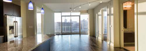 Interior view of empty AMLI Design District apartment living room and kitchen with floor to ceiling windows and city view