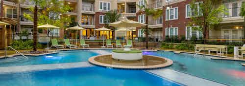 Nighttime view of AMLI Frisco Crossing apartments swimming pool area with lounge seating, umbrellas and palm trees