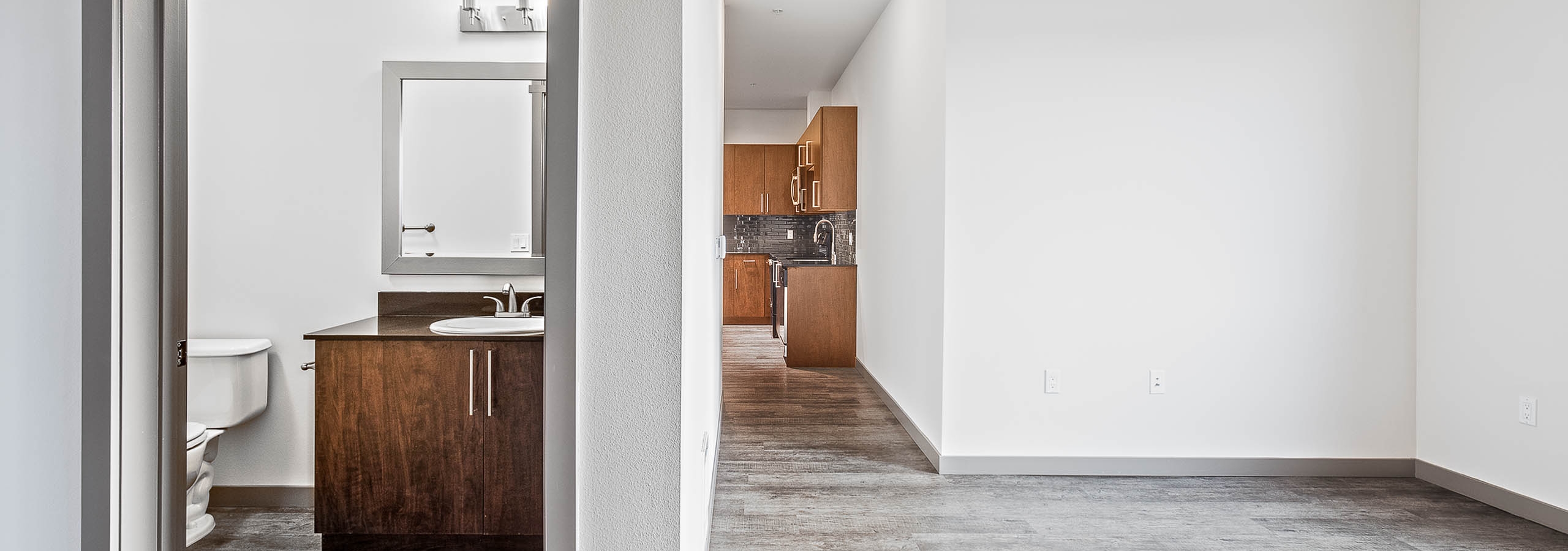 Interior view of bathroom and kitchen from the living room of a AMLI Mark24 apartment with dark cabinets light floors