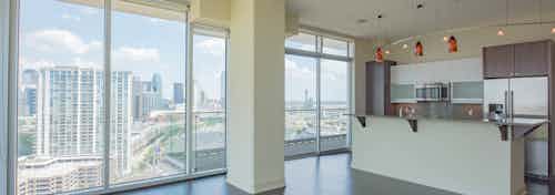 Interior view of empty AMLI Design District apartment living room and kitchen with floor to ceiling windows and city view