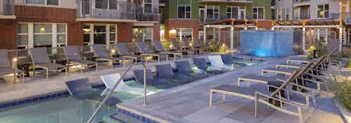 Nighttime view of the pool at AMLI Riverfront green apartments with several lounge chairs and a tiled waterfall fountain