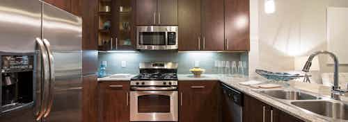 AMLI Uptown apartment kitchen with dark brown solid and glass shaker cabinets and tile backsplash and stainless appliances