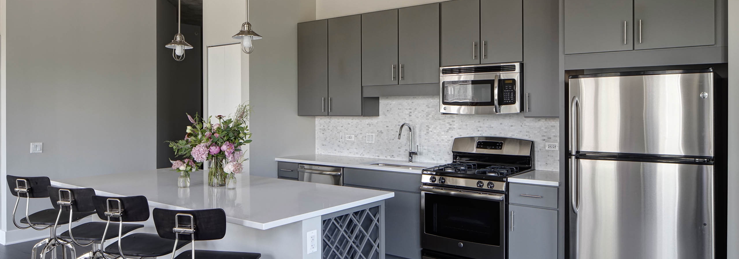 An AMLI Lofts kitchen which is painted gray and white and has an island with quartz countertops and four black bar stools