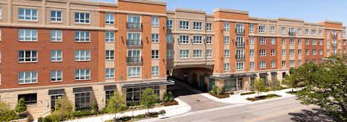 Daytime exterior view of AMLI River Oaks brick apartment building entrance with black awnings and tree-lined street