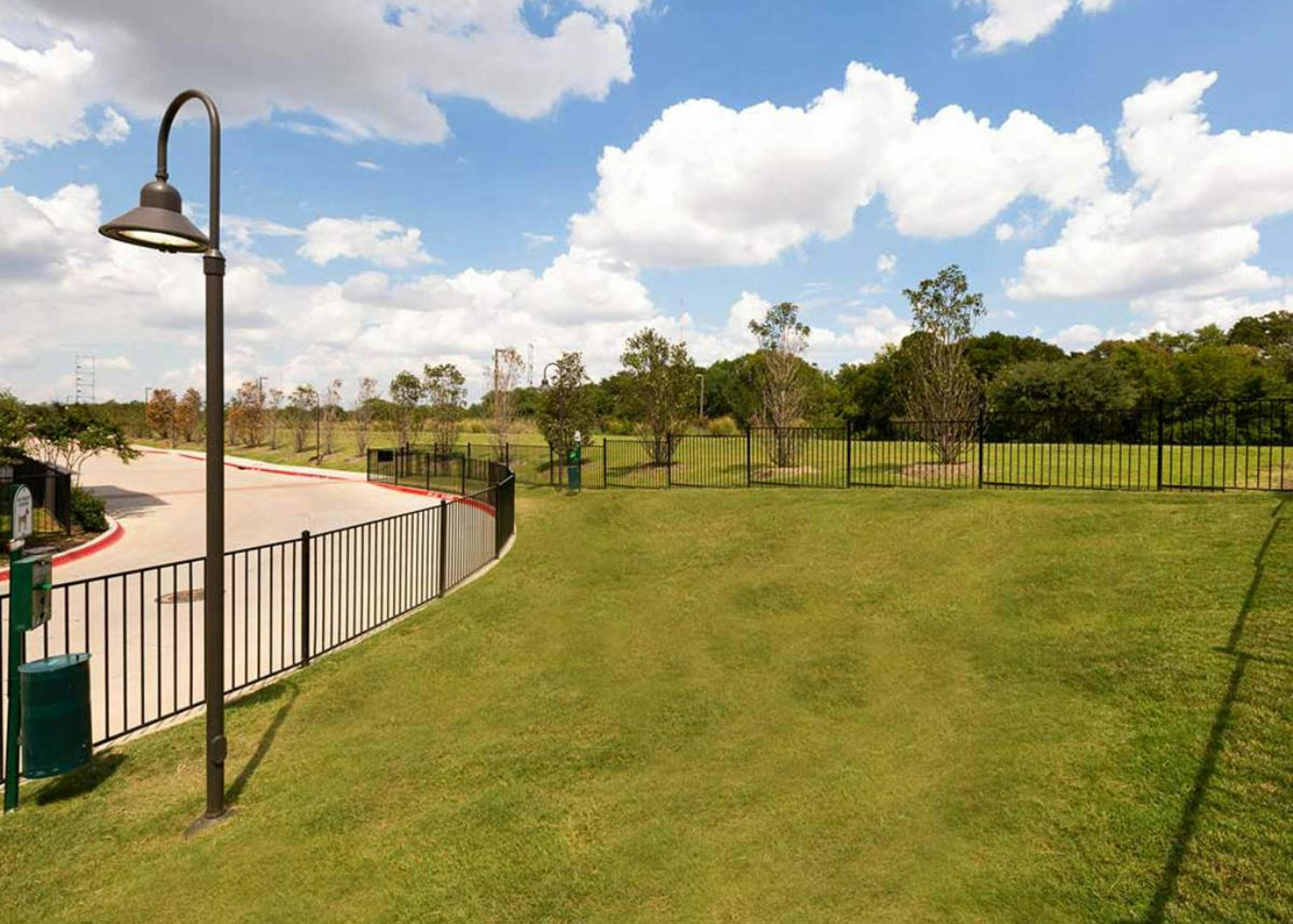  AMLI Campion Trail apartments fenced in paw park with green grass and pet waste stations and blue sky with puffy clouds above