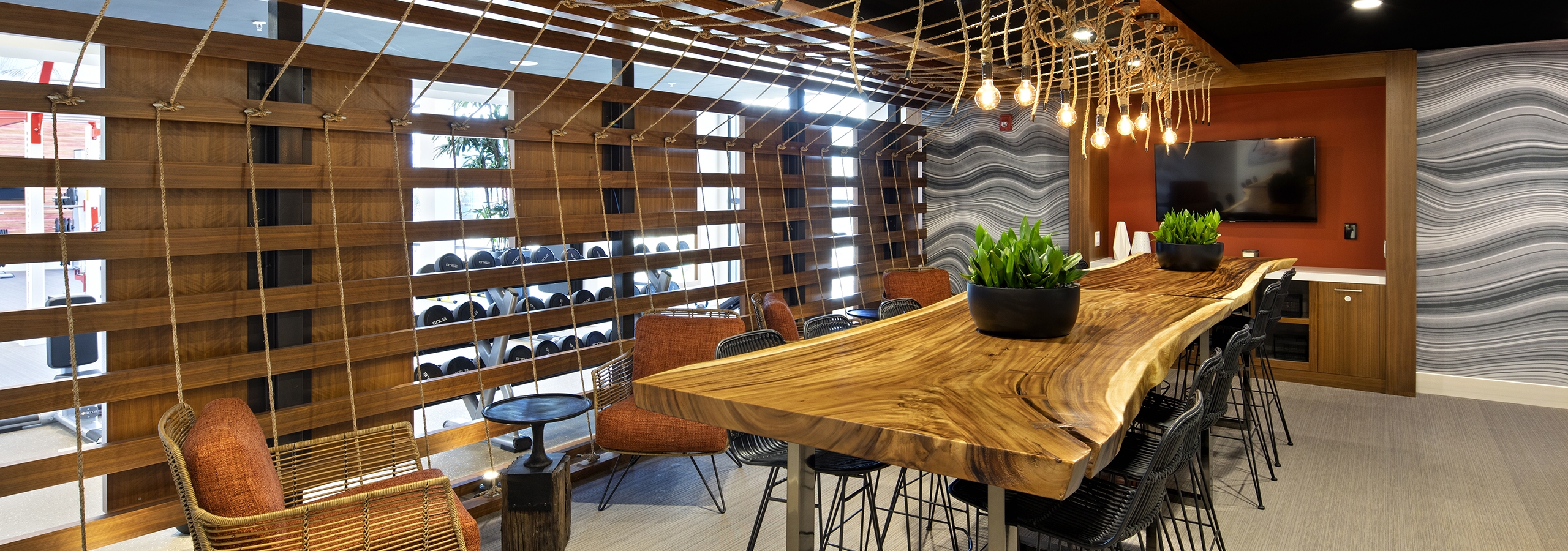 Interior of AMLI Marina Del Rey apartment workout rest area with live edge wood slab table and bulb rope pendant lighting