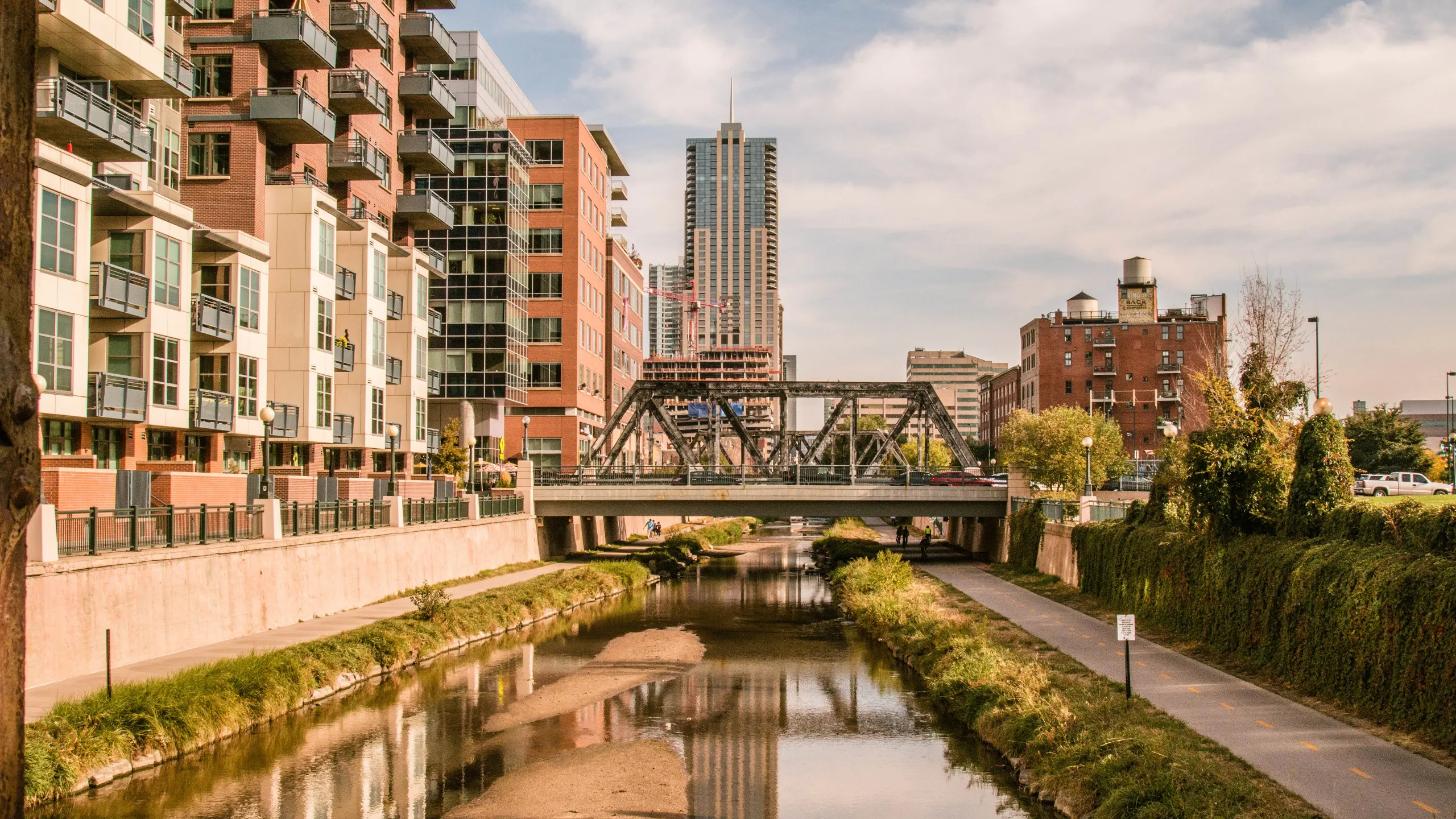 An exterior view of the South Platte River with a pedestrian bridge crossing from the urban area to a park