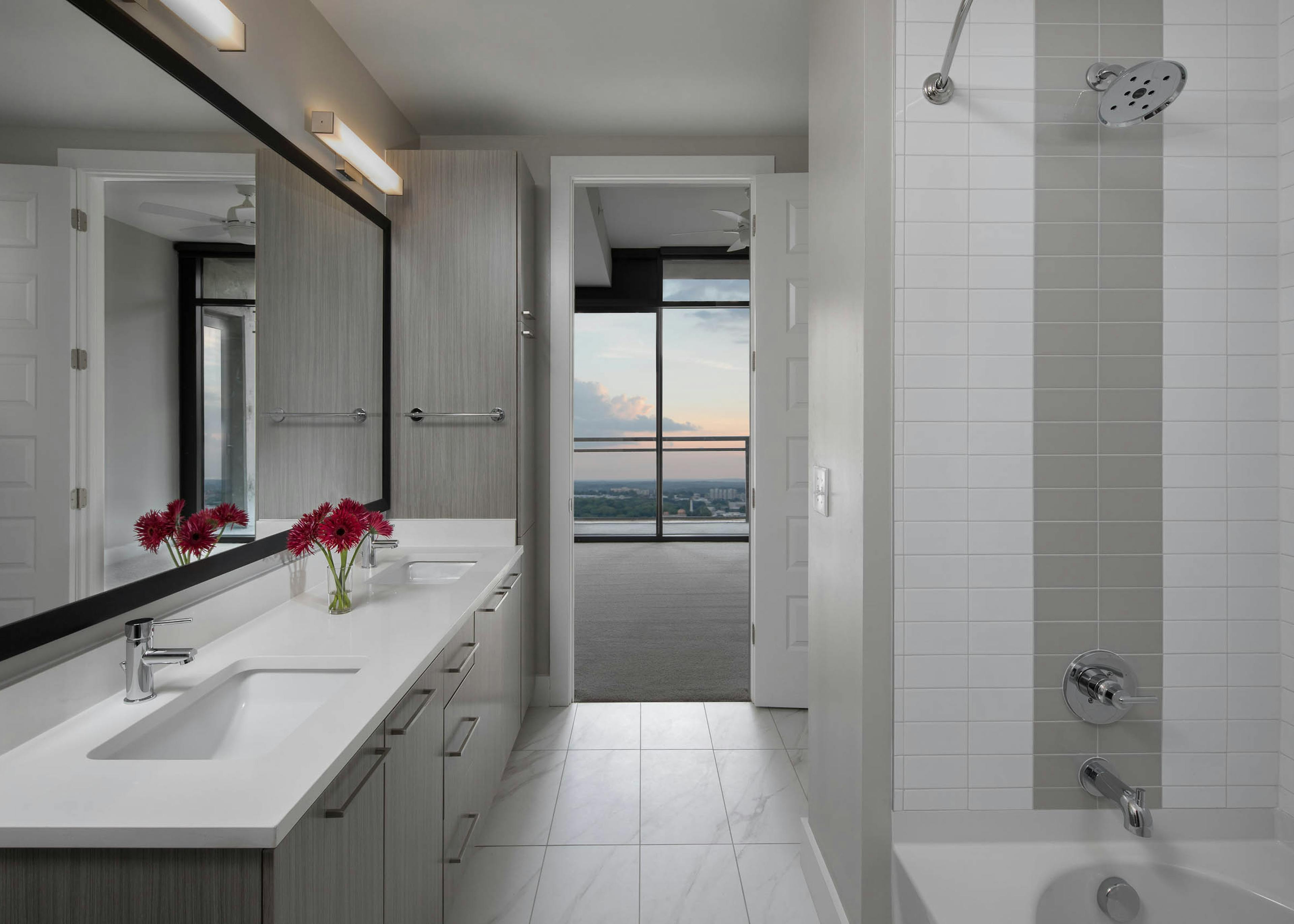 Interior of bathroom at AMLI Arts Center with double vanity sink and white tile flooring with a grey and white tiled bathtub