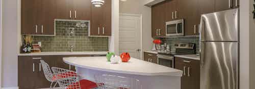 Interior view of AMLI Sawgrass Village apartment island kitchen with stainless steel appliances and dark wood cabinetry