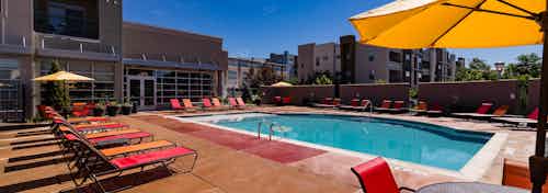 A pool at AMLI Arista apartments with several brightly colored lounge chairs and umbrellas with a view of the clubhouse