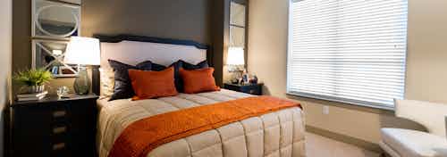 Interior view of bedroom at AMLI River Oaks apartment building with bed, two nightstands with lamps and window with blinds
