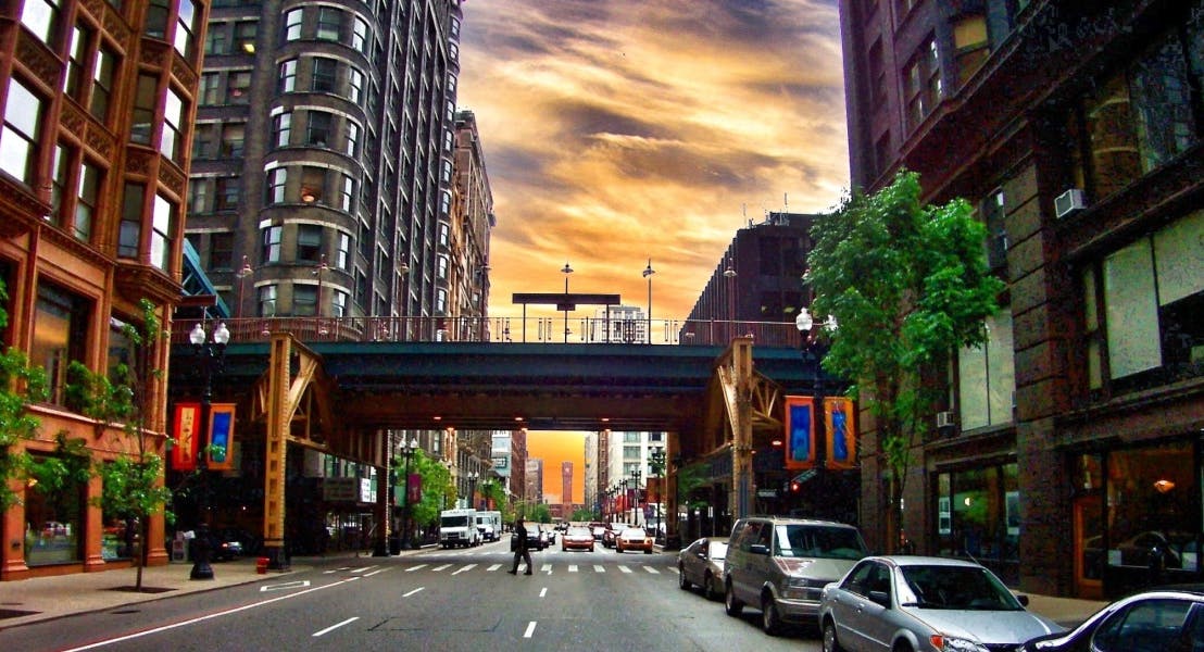 Chicago city view of the sun setting over the tall buildings, parked cars and walking pedestrians near AMLI 900 in South Loop