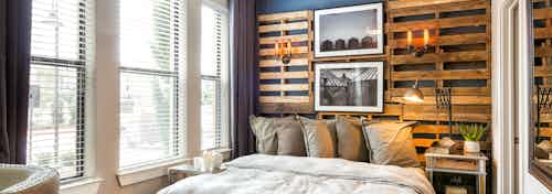 Interior view of AMLI Campion Trail studio apartment bedroom area with bed and night stand and large windows