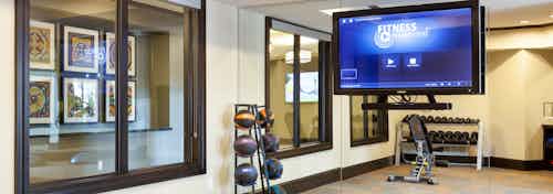 Interior of workout room at AMLI Campion Trail apartments with fitness on demand on big screen TV, dumbbells and balls