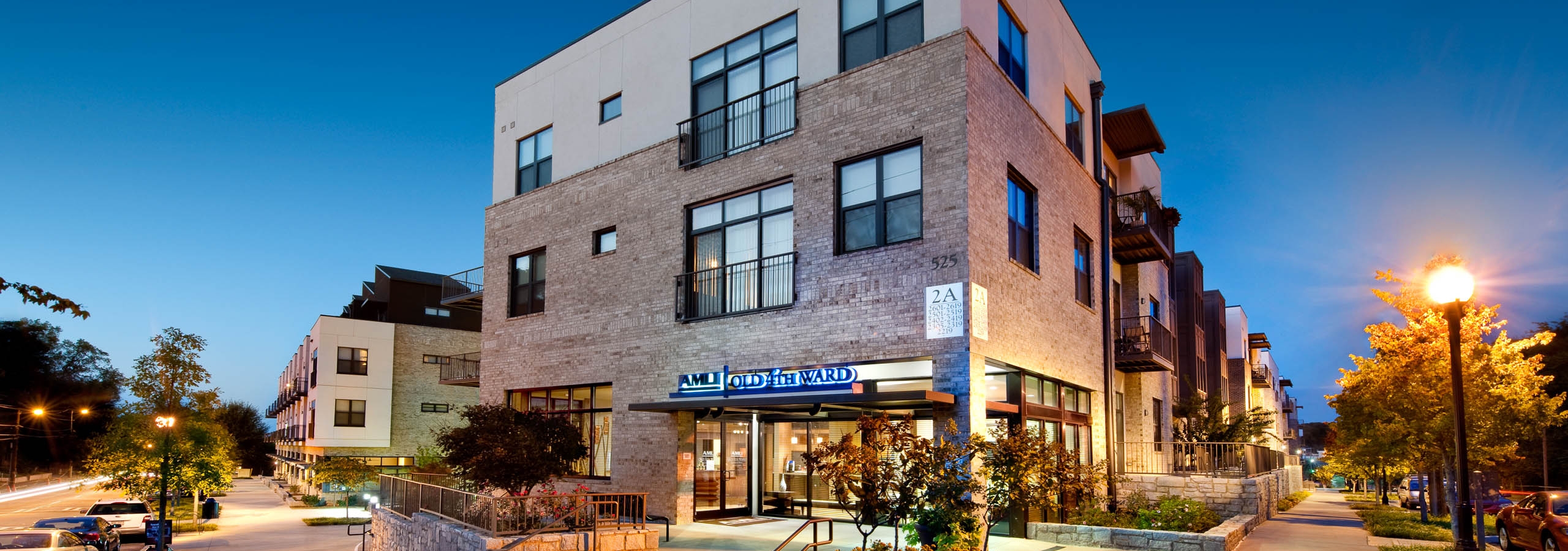 Nighttime exterior view of AMLI Old 4th Ward apartment brick facade with sign above building entrance and trees
