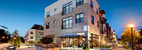 Nighttime exterior view of AMLI Old 4th Ward apartment brick facade with sign above building entrance and trees