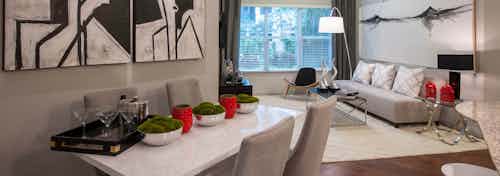 Interior view of dining room with white table and chairs looking into living room with large window at AMLI Uptown apartments