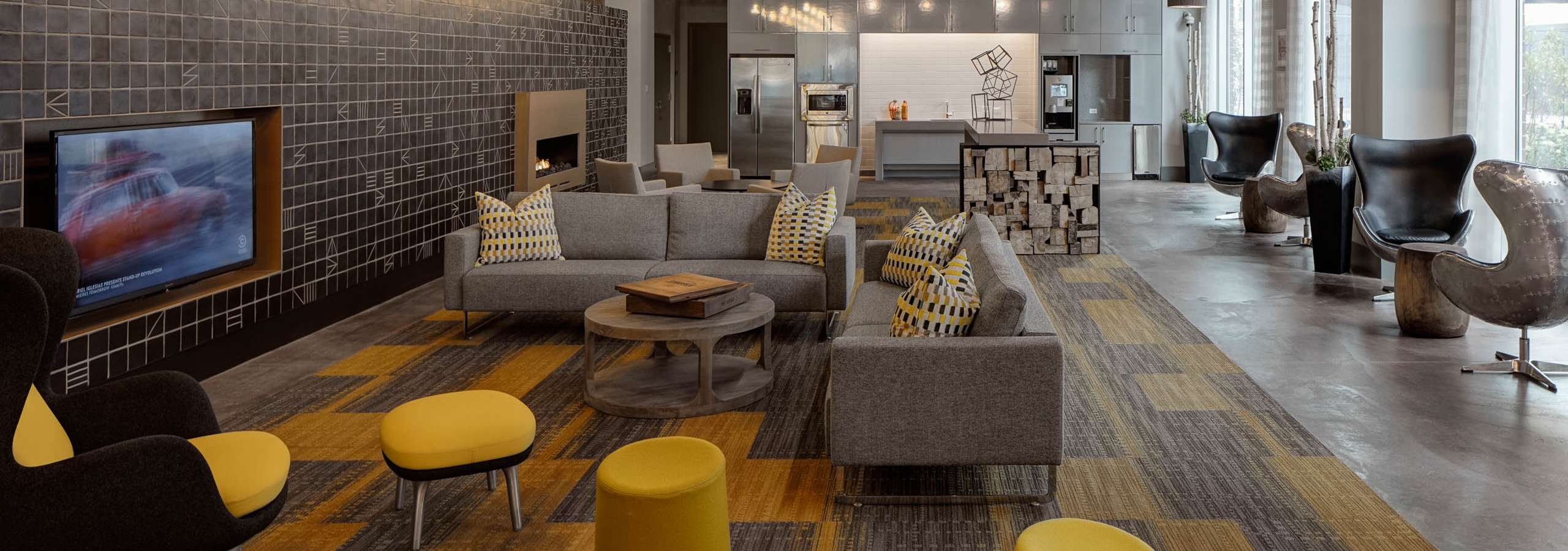 The resident clubroom at AMLI Lofts which has multiple seating areas and a large TV with vibrant yellow accents in the decor