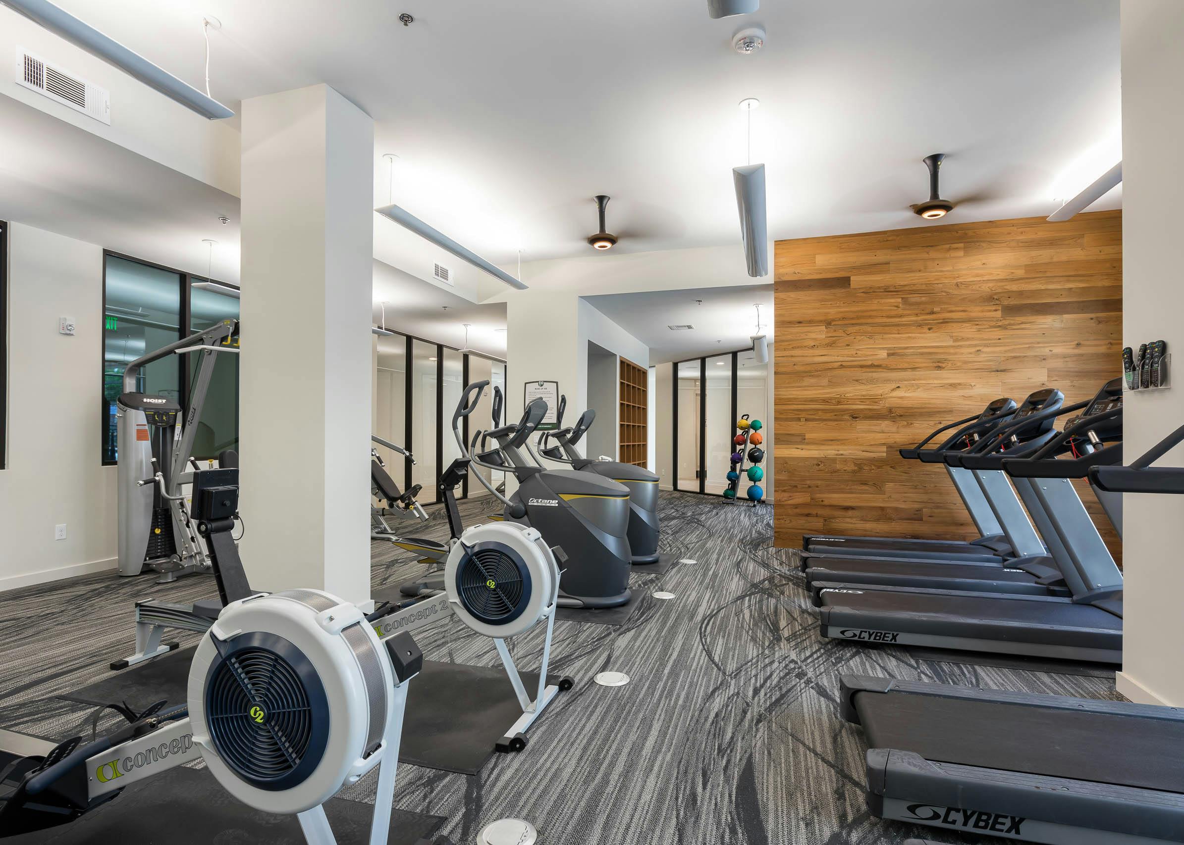 Fitness center at AMLI Frisco Crossing apartments with treadmills and other cardio machines and wood wall and white pillars