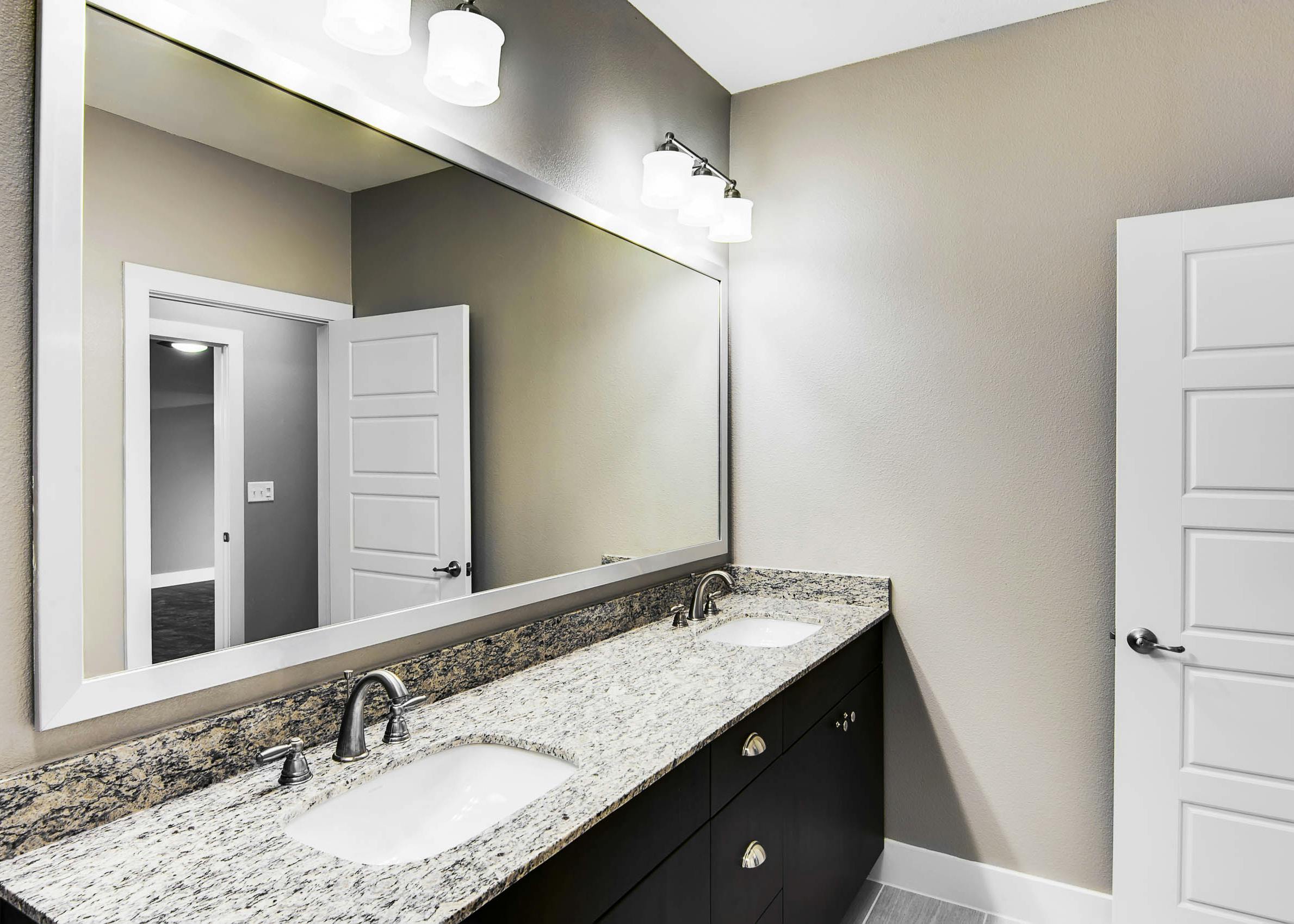Interior of AMLI Frisco Crossing apartment bathroom with granite double vanity and espresso cabinets and large framed mirror