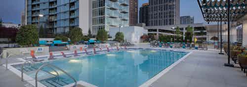 Exterior view of rooftop pool with lights on at AMLI Arts Center at dusk with view of city buildings in the background