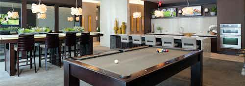 Interior view of resident lounge with billiards table, kitchen and various seating at AMLI River Oaks apartment building