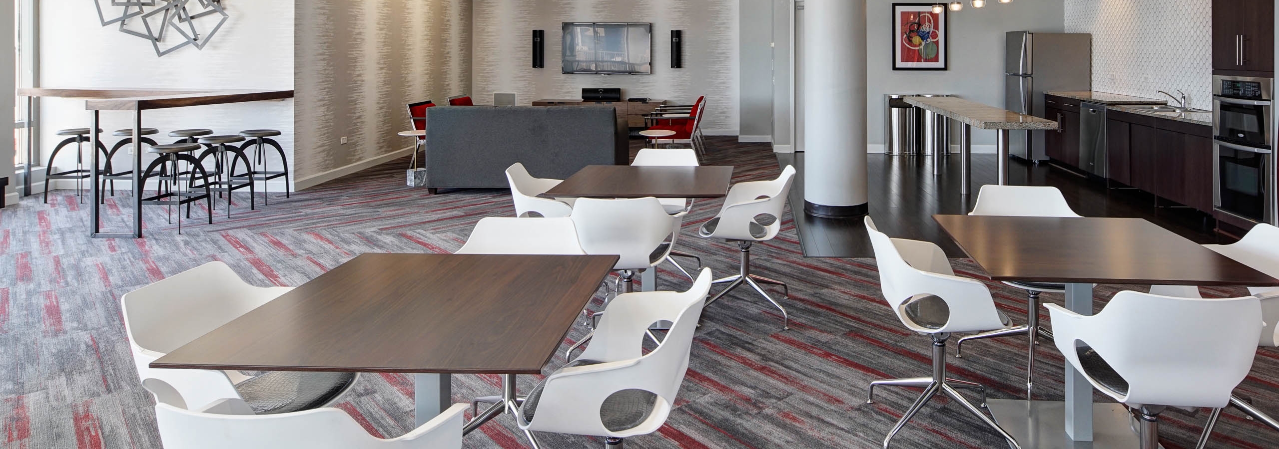 Rooftop lounge at AMLI 900 decorated in neutral colors with red accents, featuring various seating options and a kitchenette