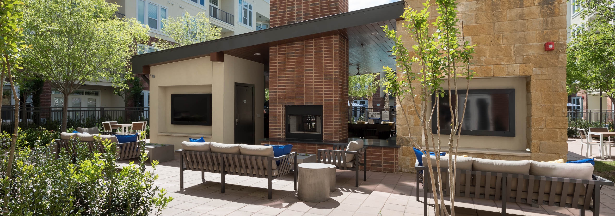 Daytime view of AMLI Frisco Crossing outdoor living room with fireplace, big screen TVs, seating and landscaping