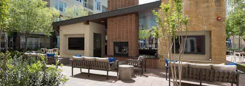 Daytime view of AMLI Frisco Crossing outdoor living room with fireplace, big screen TVs, seating and landscaping