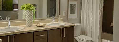 AMLI Uptown apartment bathroom with double vanity, large mirror, dark wood cabinets with designer hardware and garden tub