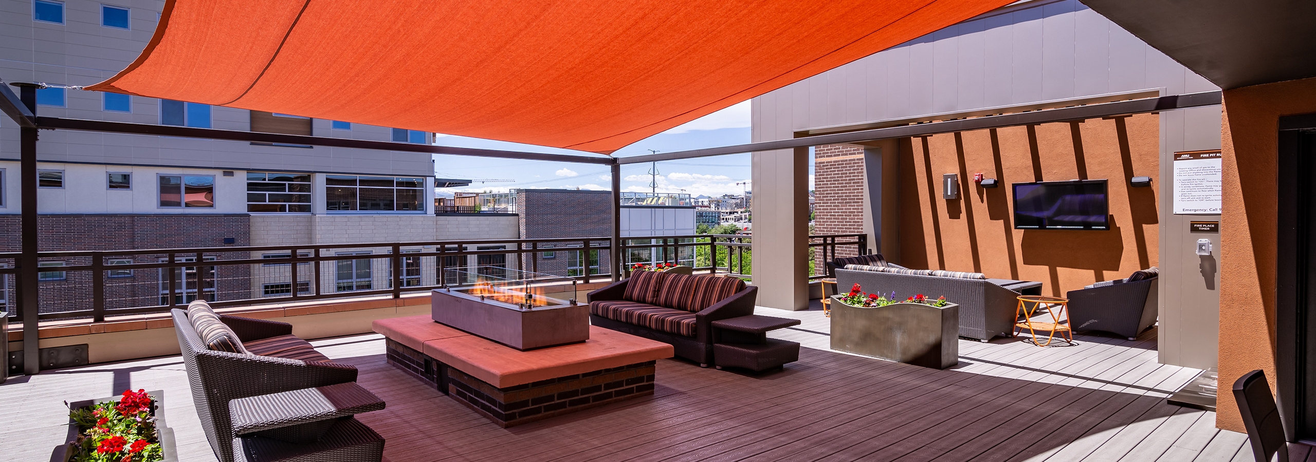 The rooftop at AMLI Riverfront Park apartments featuring a television and couches and a fire pit and an orange overhead shade
