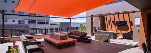 The rooftop at AMLI Riverfront Park apartments featuring a television and couches and a fire pit and an orange overhead shade
