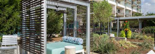 Daytime view of cabana with bed and small table and lush landscaping at AMLI Design District apartment building rooftop