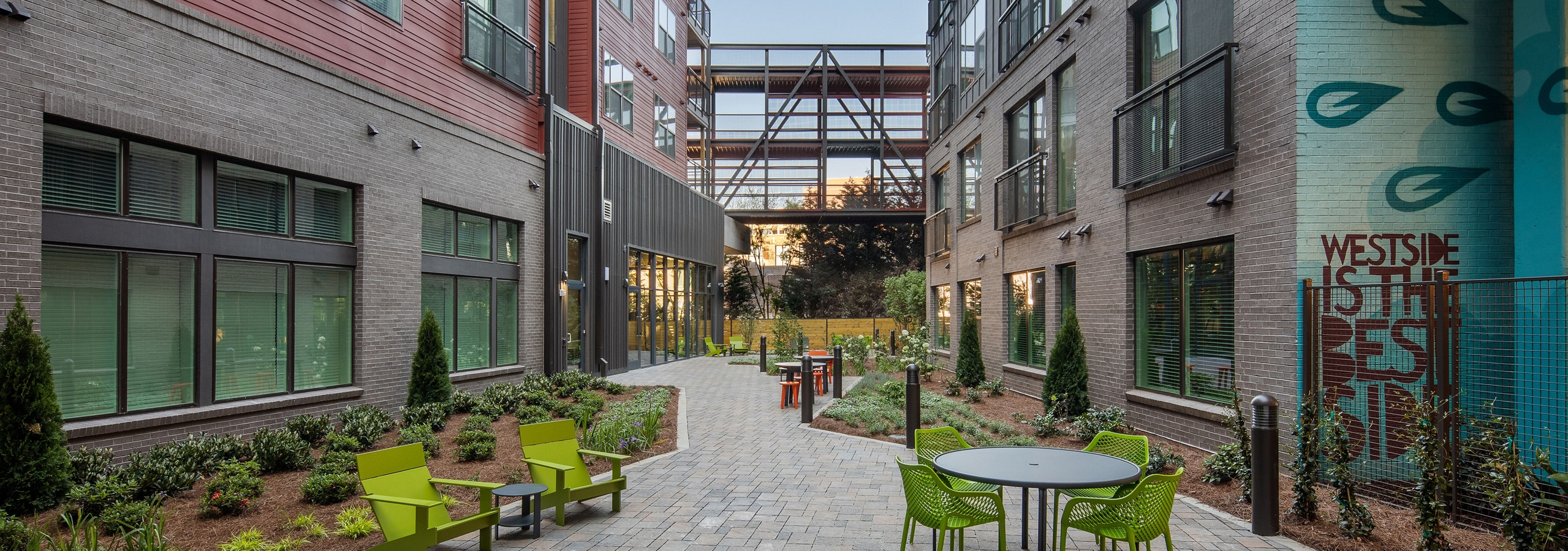 Daytime exterior view of AMLI Westside landscaped courtyard with various colorful seating options on a brick pathway