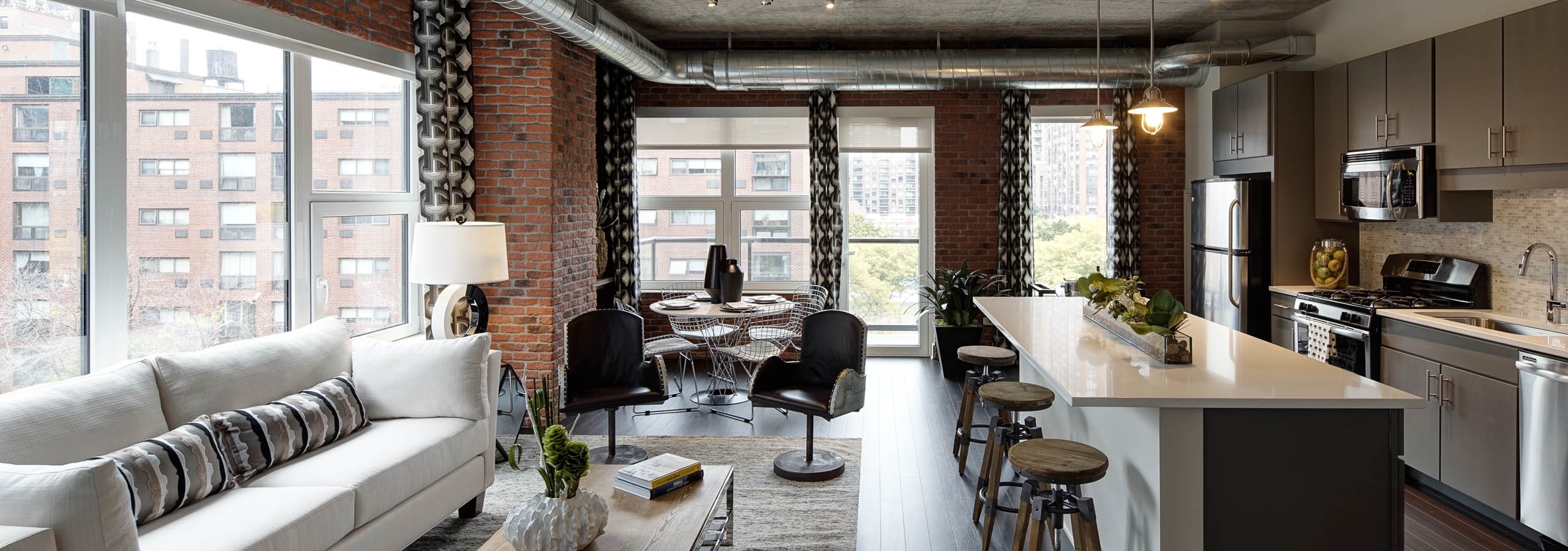 Interior view of living room and kitchen at AMLI Lofts featuring exposed brick wall with dark flooring and quartz countertops