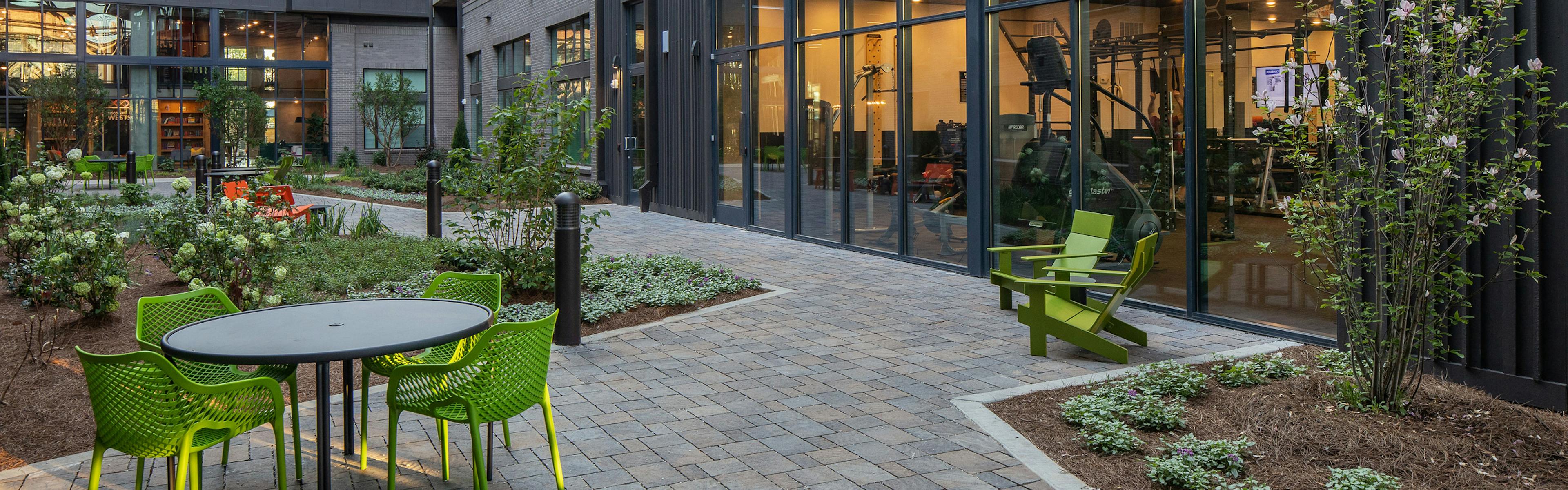 AMLI Westside courtyard with table and green chairs on brick walkway next to large windows looking into fitness center