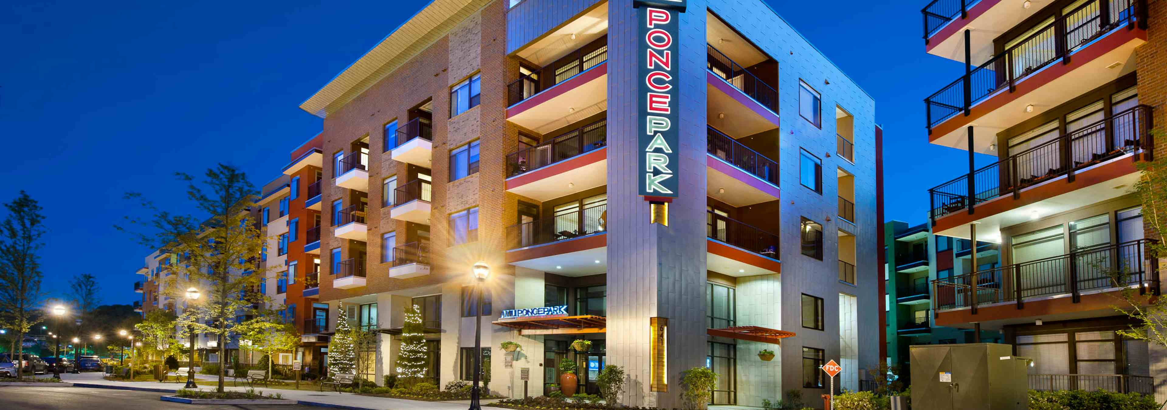 Nighttime exterior view of AMLI Ponce Park apartment community brick facade with sign above building entrance and trees