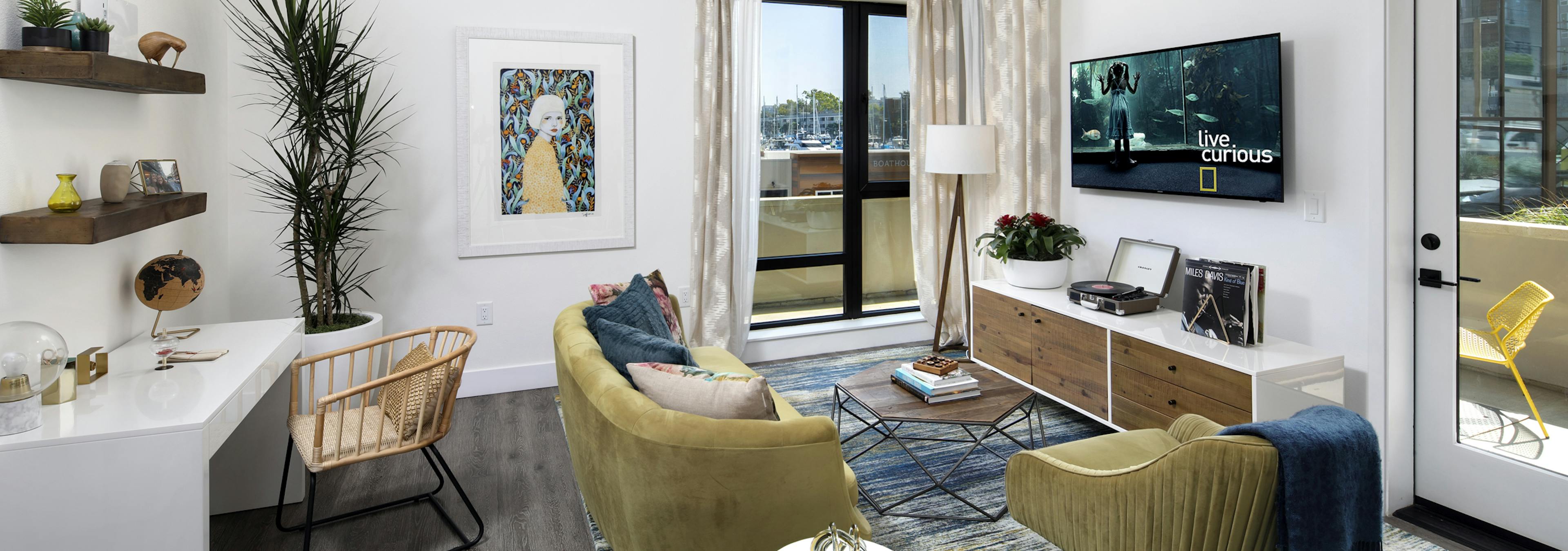 Interior of AMLI Marina Del Rey model living room with couch, coffee table and desk in front of large window facing marina