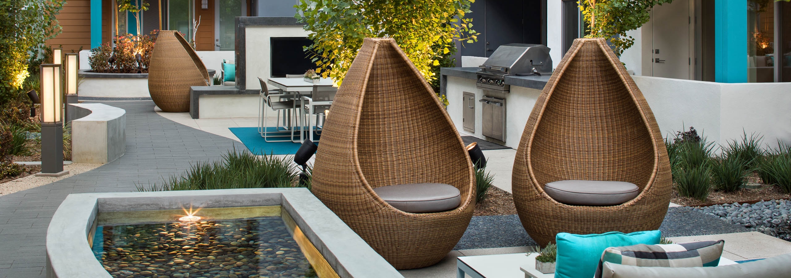 Daytime view of outdoor courtyard at AMLI Uptown Orange with teardrop wicker chairs and reflection ponds and grill stations