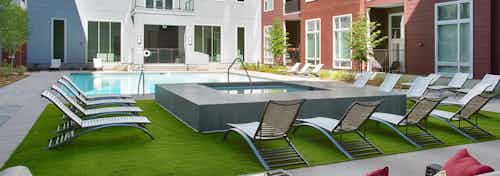 Exterior view of the pool area at AMLI Denargo Market with a hot tub and lounge chairs on turf with apartment in background
