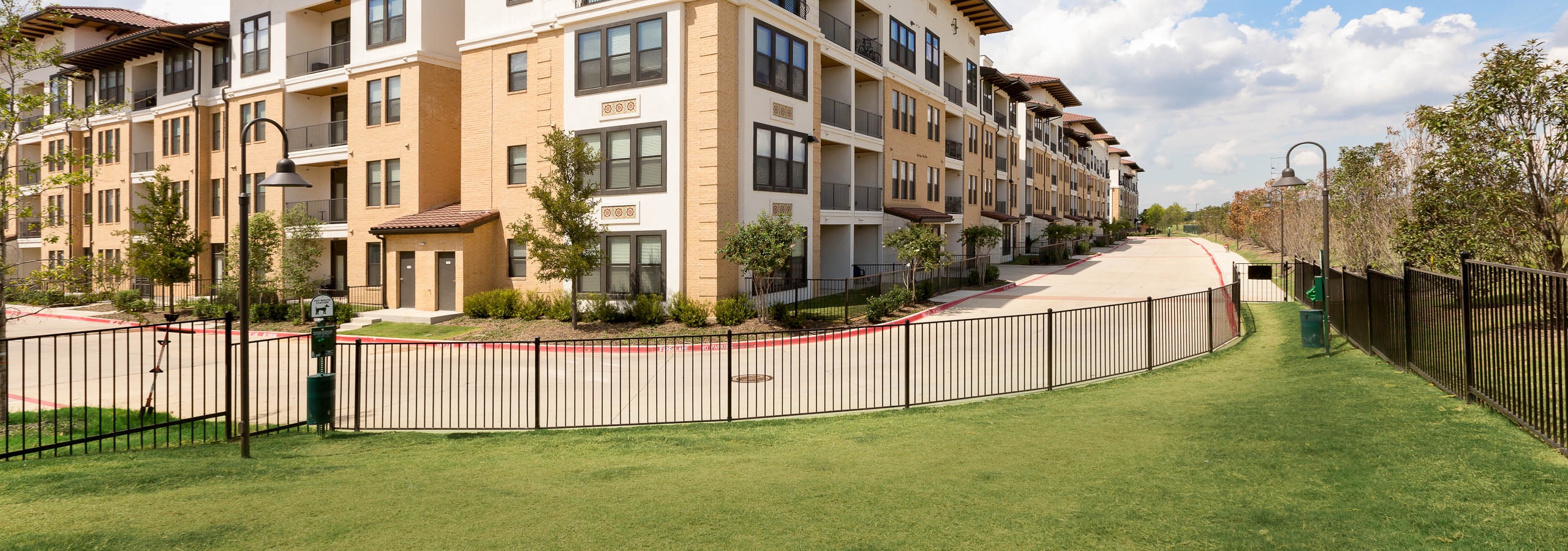 Daytime view of paw park with fence, green grass and pet waste stations outside of AMLI Campion Trail apartment building