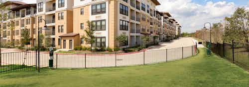 Daytime view of paw park with fence, green grass and pet waste stations outside of AMLI Campion Trail apartment building