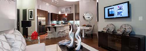 View from AMLI Uptown apartment living room with couch and coffee table and TV into island kitchen and dining area