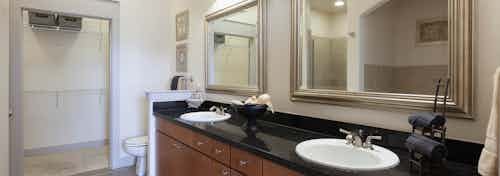 Interior view of AMLI Las Colinas apartment bathroom with black granite double vanity, wood cabinets and walk-in closet