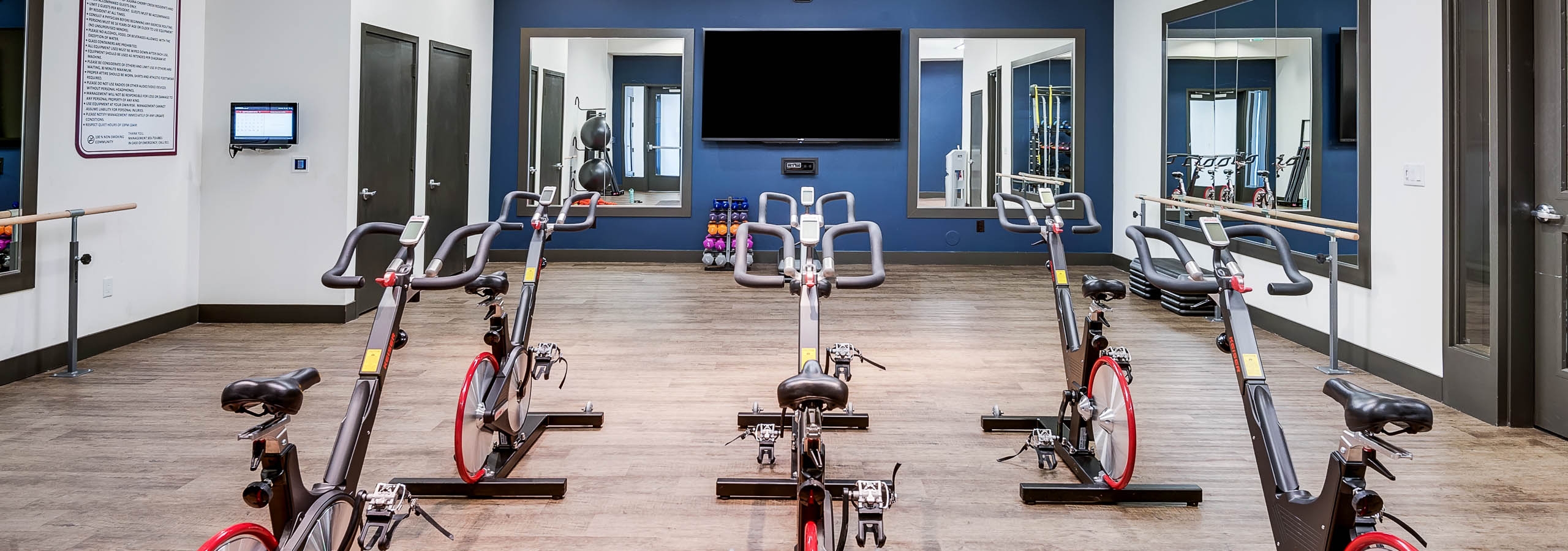 A spin studio at AMLI Cherry Creek apartments with multiple stationary bikes and a large television and hard wood floors