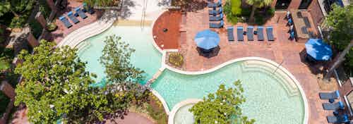 Daytime aerial view of curvy swimming pool with lounge chairs and umbrellas at AMLI Memorial Heights apartment building