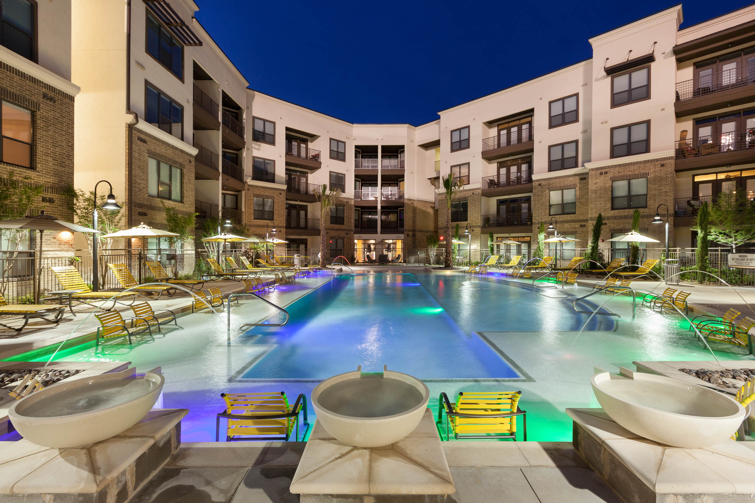 Nighttime view of swimming pool with yellow lounge furniture and fountains at AMLI at the Ballpark apartment building