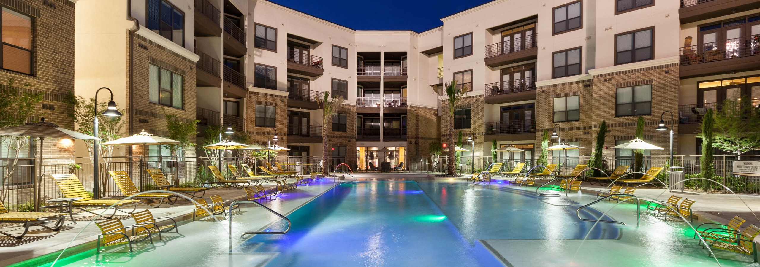 Nighttime view of swimming pool with yellow lounge furniture and fountains at AMLI at the Ballpark apartment building