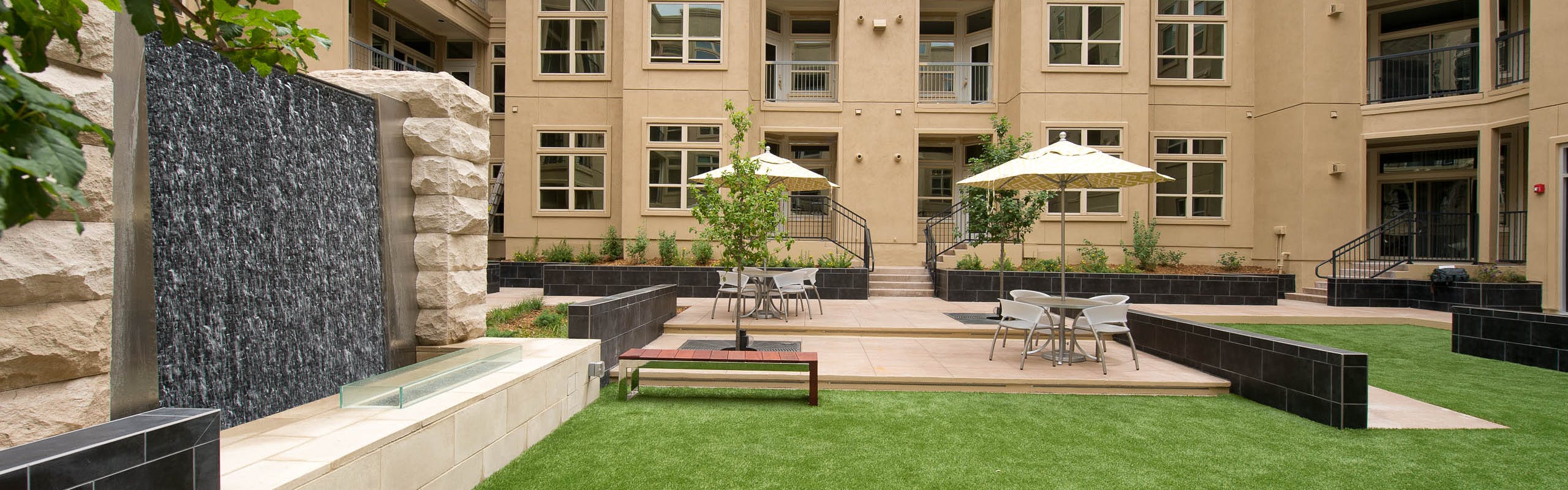 Daytime view of AMLI RidgeGate Zen garden with cascading stone waterfall, turf and various seating with umbrellas and trees
