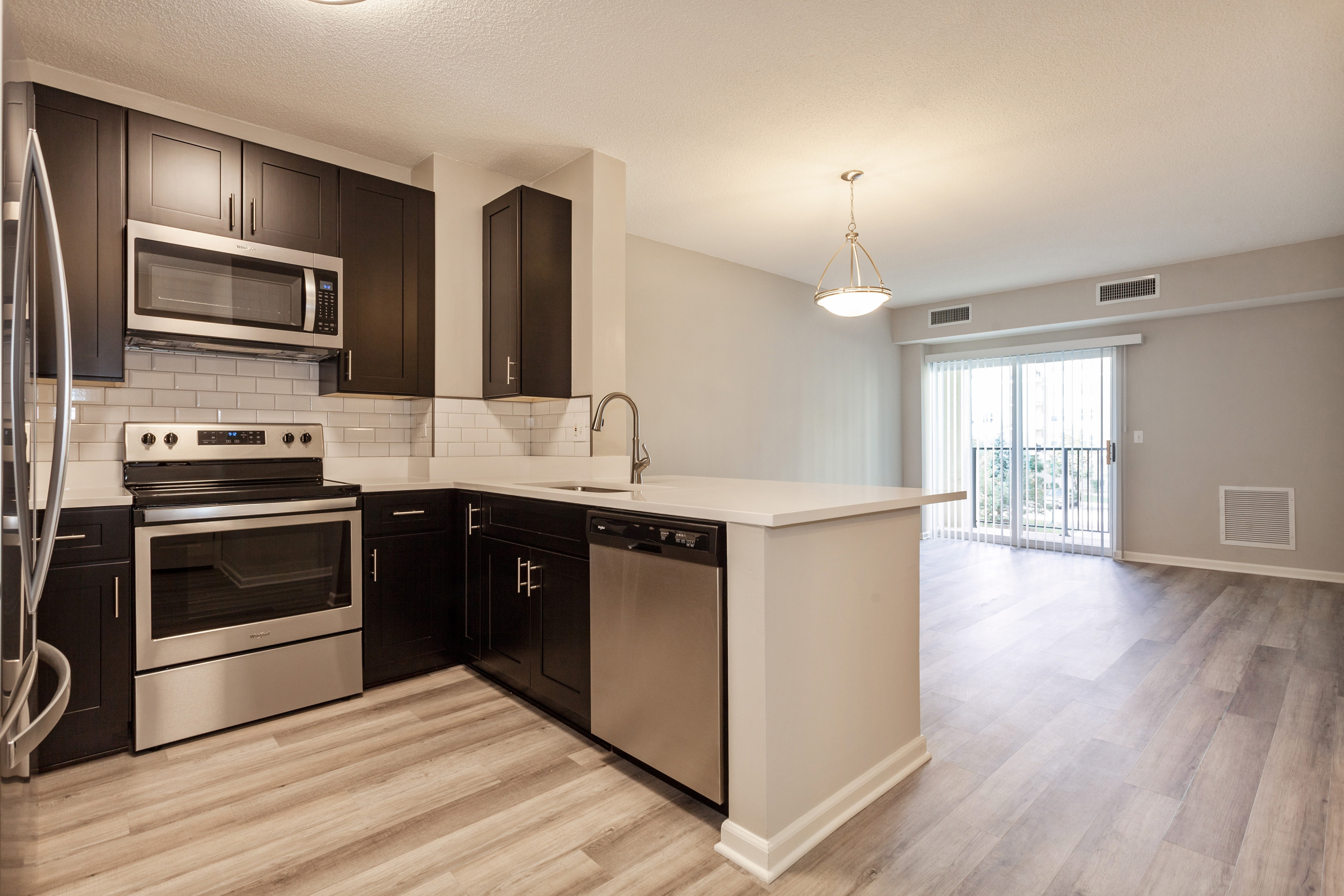 AMLI at Seven Bridges living room and kitchen with dark cabinetry and stainless steel appliances and wood-style plank floors